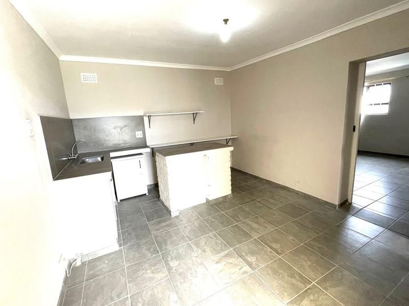 A basic, empty kitchen area featuring tiled flooring, a small sink unit, and built-in shelving, offering a blank canvas for potential renovation.