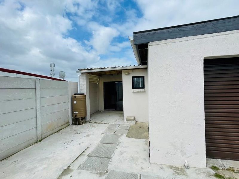 Rear exterior view featuring a concrete paved courtyard, a covered patio area, a water tank, and access to the garage.