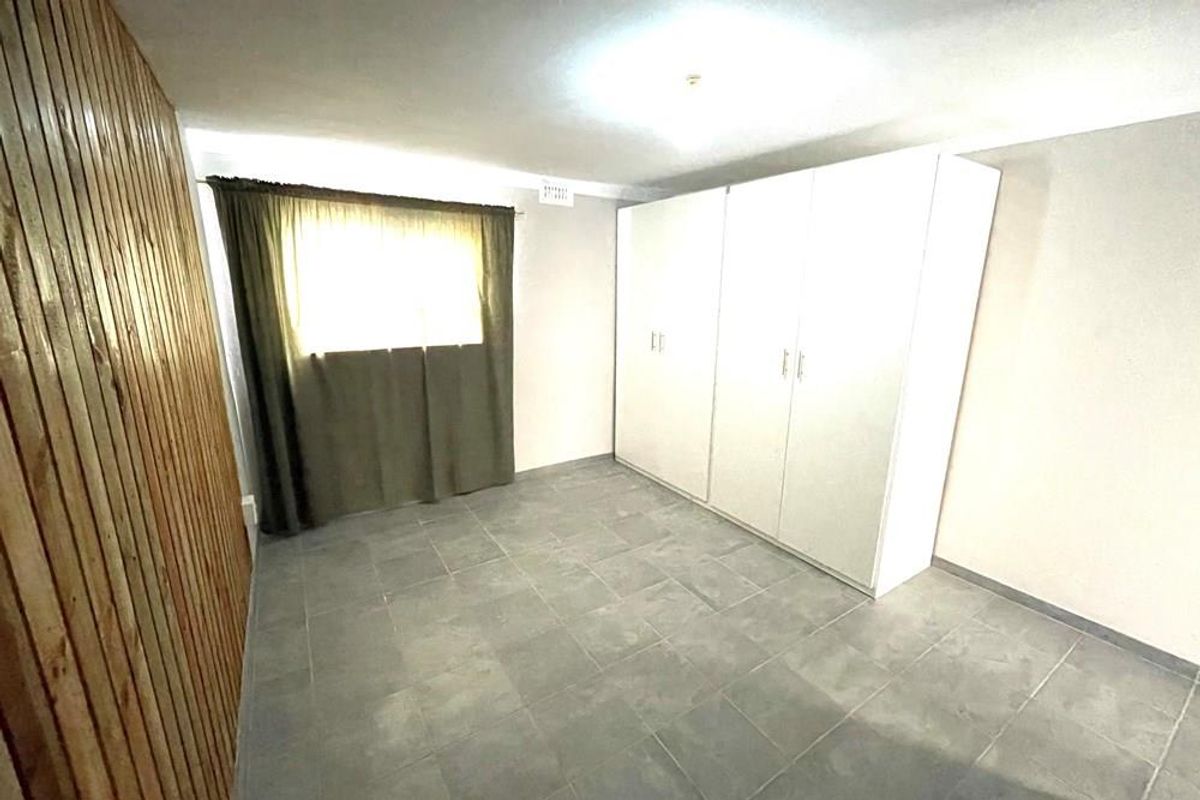A simple bedroom featuring tiled flooring, a built-in wardrobe, and a decorative timber-paneled feature wall.
