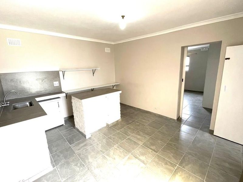 A basic, empty kitchen area featuring tiled flooring, a built-in sink, and simple counter space, offering a blank canvas for potential renovation.