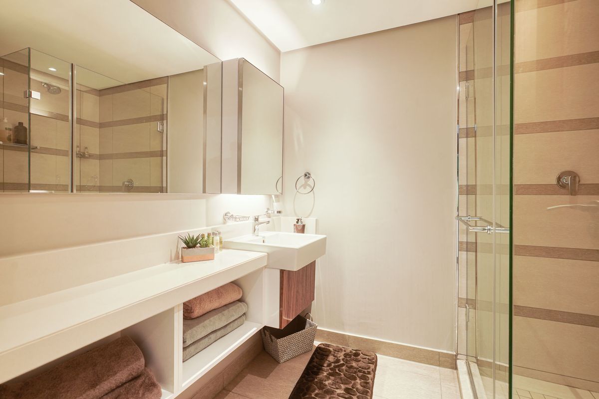 Modern bathroom featuring a floating vanity with integrated basin, large wall-mounted mirror, and a glass-enclosed shower with neutral tiled finishes.