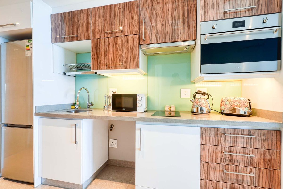 Modern kitchen featuring wood-grain and white cabinetry, stone countertops, a glass splashback, built-in oven, and integrated hob.