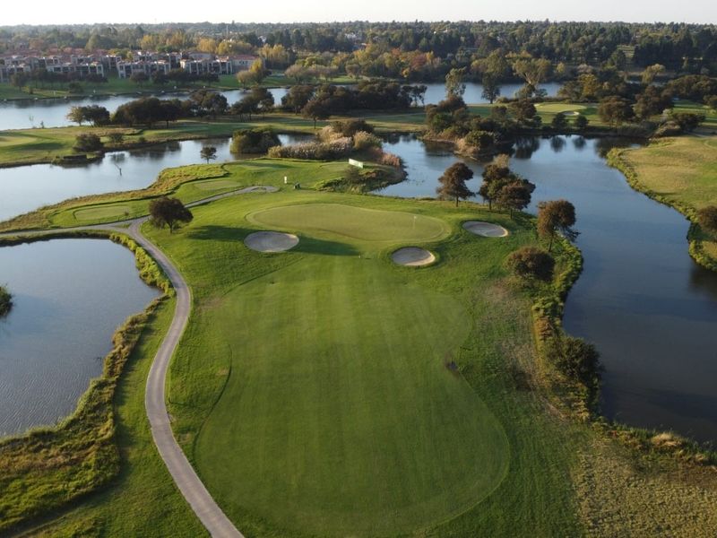 An aerial view of a well-maintained golf course hole featuring a green surrounded by water hazards and sand bunkers.