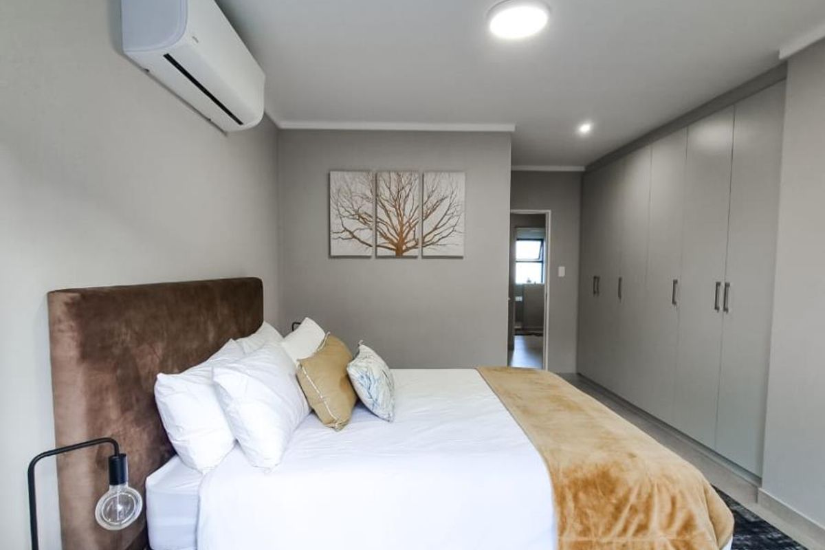 A well-maintained bedroom featuring built-in floor-to-ceiling wardrobes, tiled flooring, and a wall-mounted air conditioning unit.