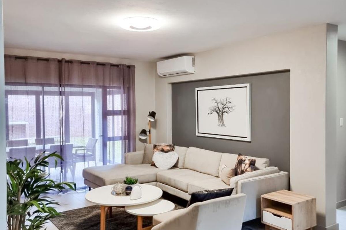 A bright and modern living room featuring tiled flooring, a wall-mounted air conditioning unit, and large sliding glass doors leading to an outdoor patio area.