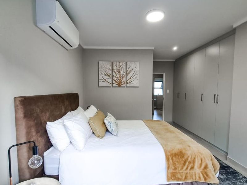 A well-maintained bedroom featuring built-in floor-to-ceiling wardrobes, tiled flooring, and a wall-mounted air conditioning unit.