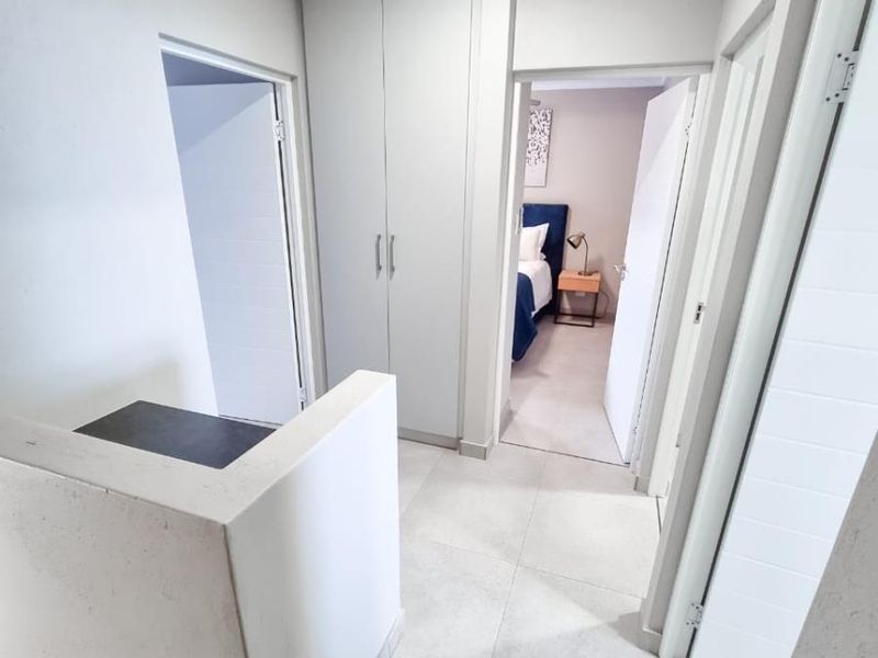 A bright, modern hallway featuring tiled flooring, built-in cabinetry, and access to adjacent bedrooms.