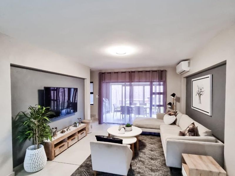 Spacious living room featuring large format floor tiles, accent walls, and sliding glass doors providing seamless access to the outdoor patio area.