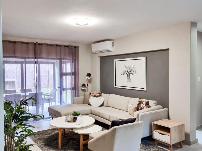 A bright and modern living room featuring tiled flooring, a wall-mounted air conditioning unit, and large sliding glass doors leading to an outdoor patio area.
