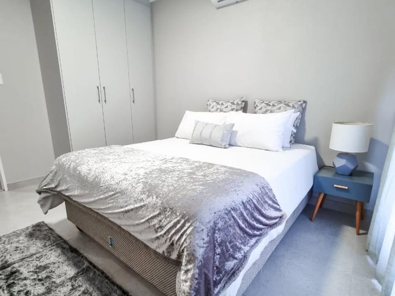 A well-maintained bedroom featuring neutral wall tones, tiled flooring, built-in cabinetry, and a wall-mounted air conditioning unit.