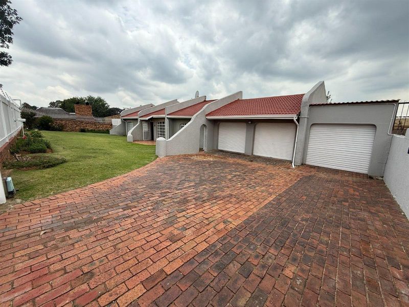 Front exterior view of the property featuring a triple garage, brick paved driveway, and a well-maintained lawn area.