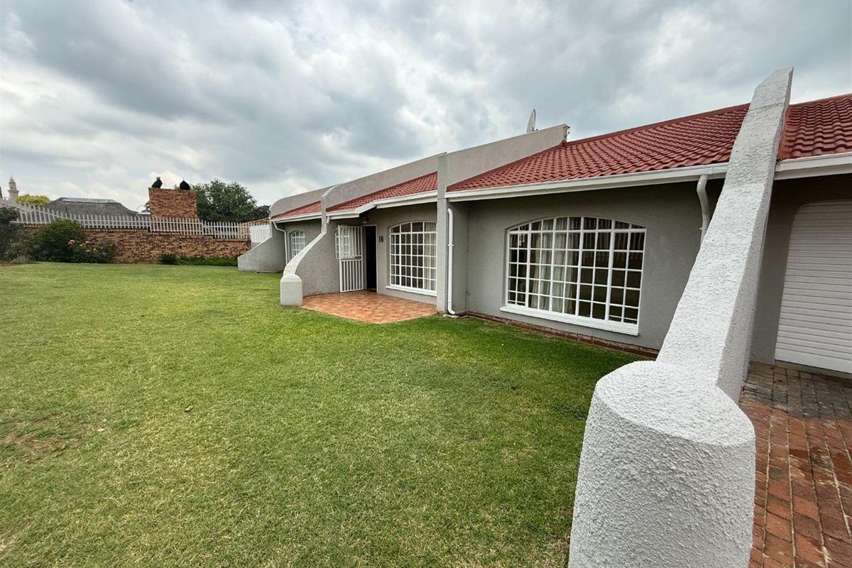 Rear view of the property featuring a spacious lawn, tiled roof, and a paved patio area with secure lattice windows.