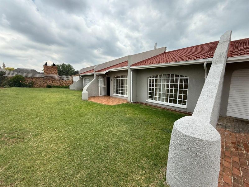 Rear view of the property featuring a spacious lawn, tiled roof, and a paved patio area with secure lattice windows.
