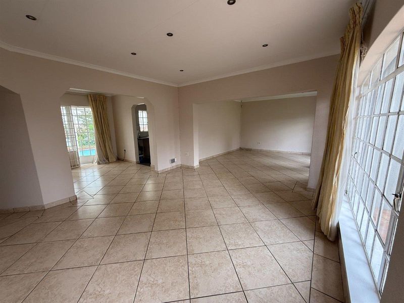 Spacious open-plan living area featuring neutral tiled flooring, recessed downlighting, and multiple archways leading to adjacent rooms and outdoor access.