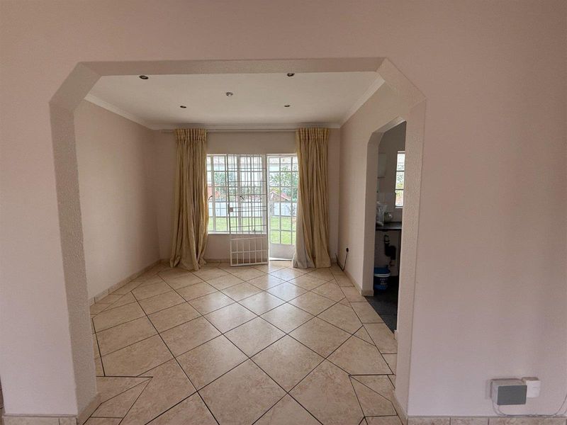 An empty living room featuring tiled flooring, recessed lighting, and a glass door providing access to the rear garden.