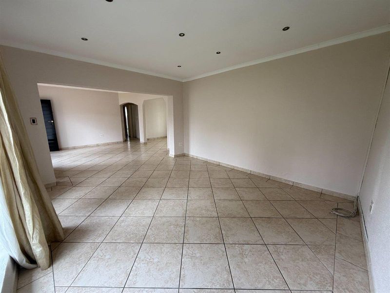 Spacious open-plan living area featuring neutral ceramic floor tiles, recessed downlighting, and coved cornicing, offering a versatile blank canvas for interior design.