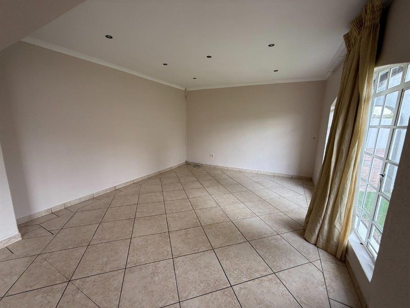 A bright, empty living room featuring neutral tiled flooring, recessed downlighting, and large windows with natural light.