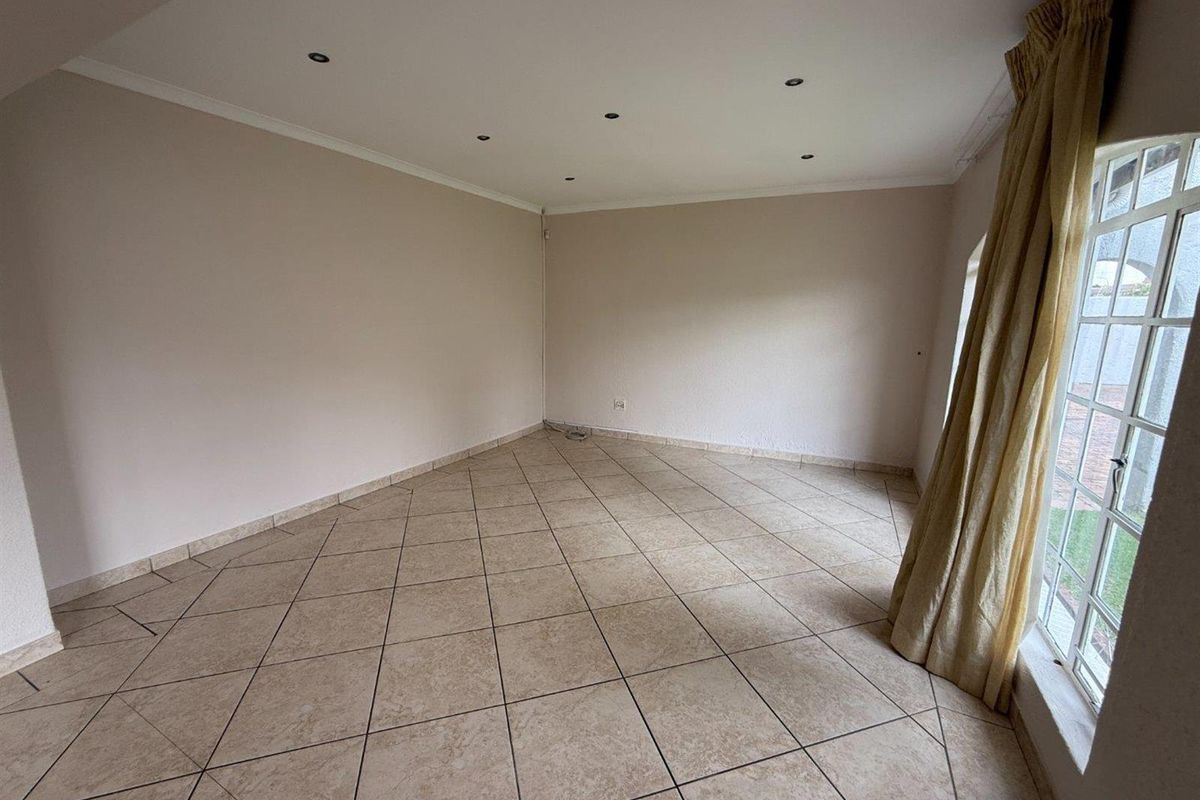 A bright, empty living room featuring neutral tiled flooring, recessed downlighting, and large windows with natural light.
