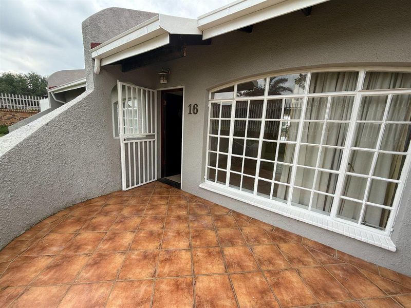 Front entrance area featuring a tiled patio, security gate, and large arched window with a textured exterior facade.