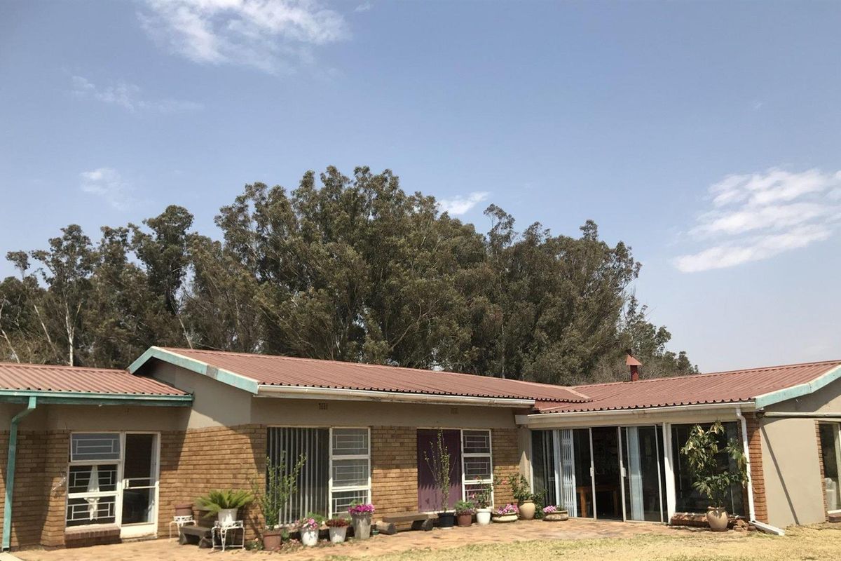 Rear view of a single-story brick farmhouse featuring a corrugated metal roof, paved patio area, and sliding glass door access.