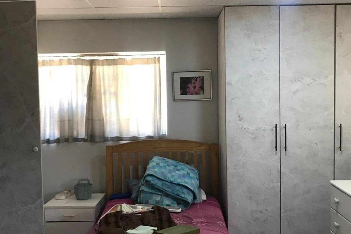A bedroom featuring built-in wardrobes with a marble-effect finish, a drop ceiling with recessed lighting, and a window providing natural light.