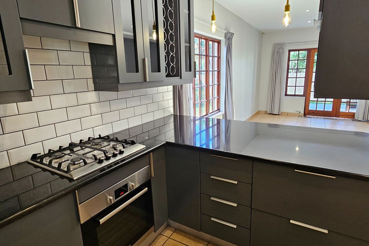 Modern kitchen featuring dark cabinetry, granite countertops, a gas hob, built-in oven, and subway tile backsplash, flowing into an adjacent living area.