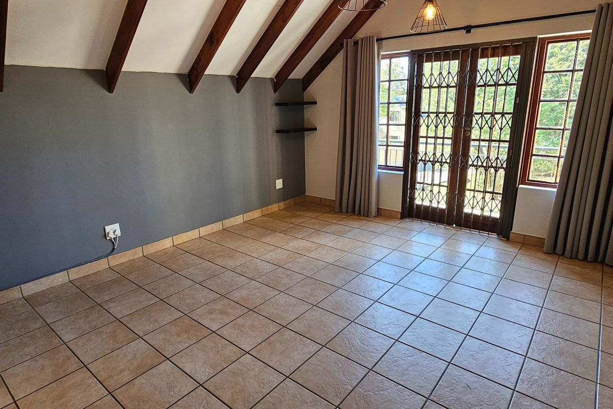 Spacious bedroom featuring exposed timber rafters, tiled flooring, built-in cupboards, and direct access to a balcony through secure french doors.