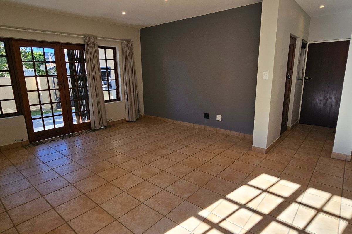 Spacious, light-filled living area featuring neutral tiled flooring, a modern accent wall, and direct access to the outdoor area through wooden framed glass doors.