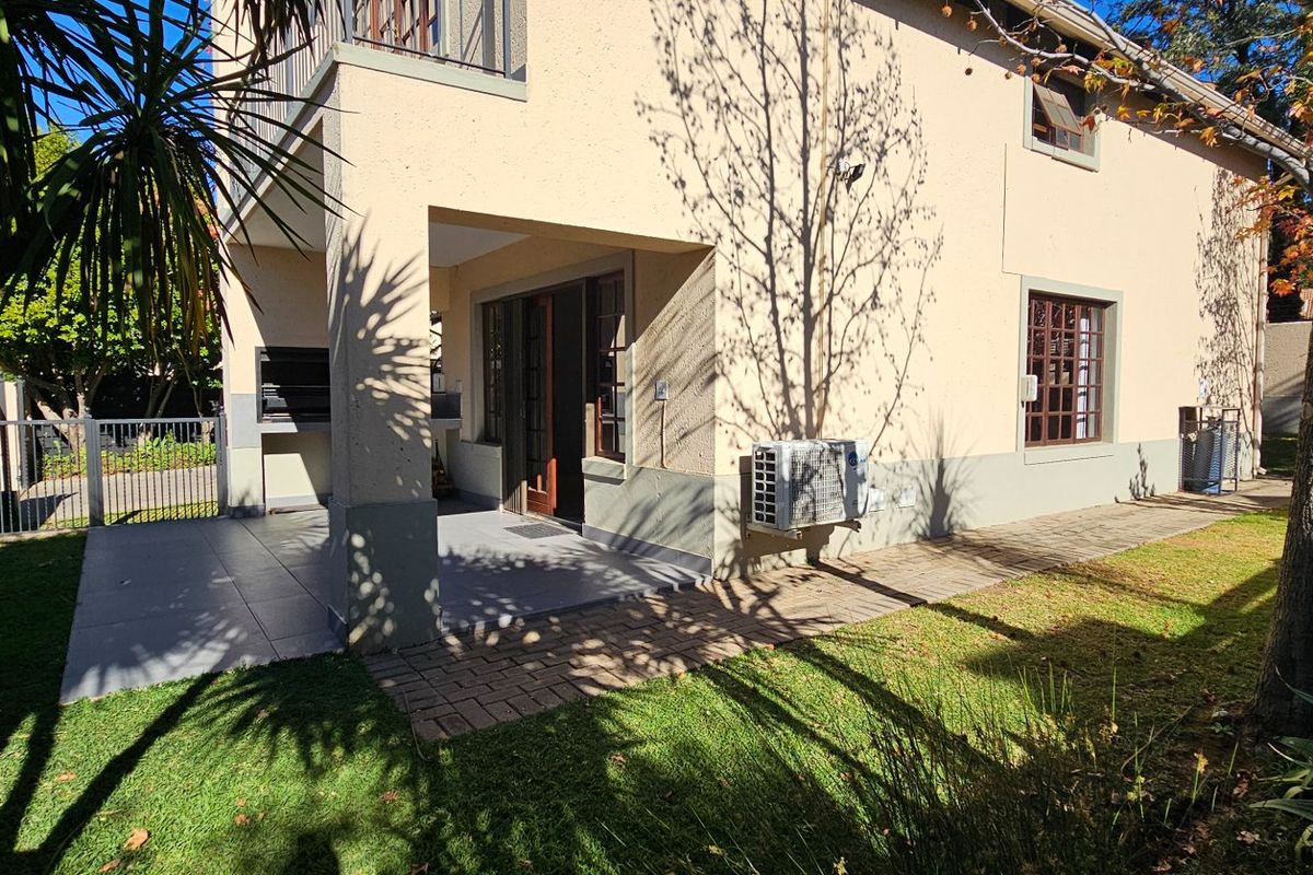Rear view of the townhouse featuring a covered patio with a built-in braai, paved walkway, and access to a private garden area.