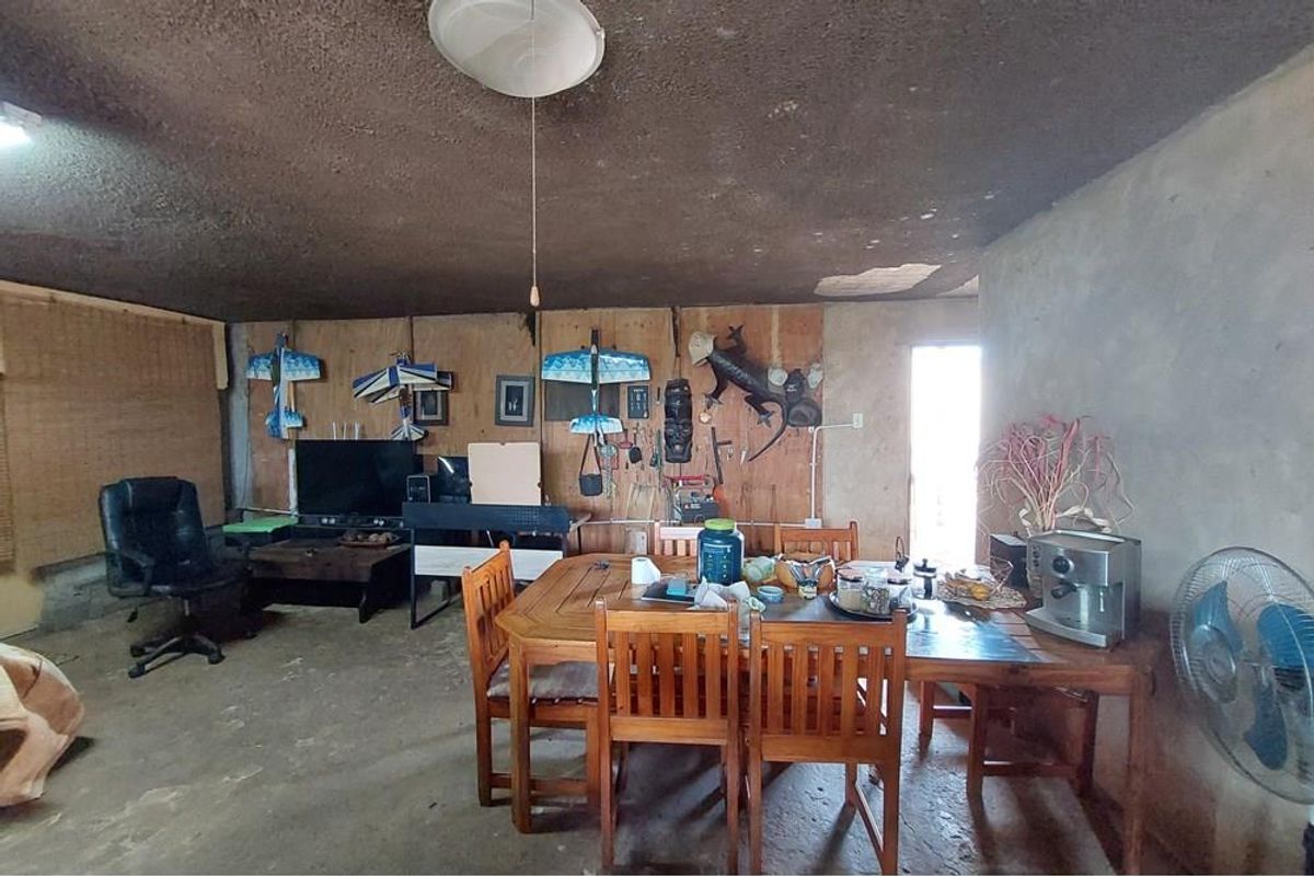 A rustic living area featuring textured ceilings, plywood wall paneling, and concrete flooring, offering a blank canvas for renovation and modernization.