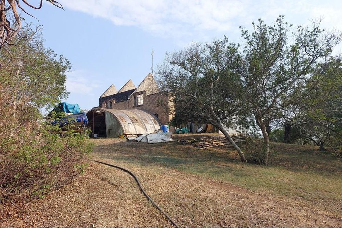 Rear view of the farm property showing the main brick structure and an adjacent arched metal outbuilding on a sloped landscape.
