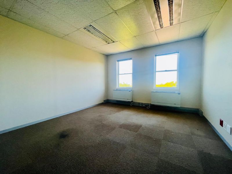 An empty commercial office space featuring carpeted flooring, suspended ceiling with recessed lighting, and wall-mounted HVAC units.