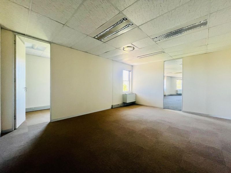An empty, open-plan office space featuring a suspended ceiling, recessed lighting, carpeted flooring, and an integrated HVAC unit.