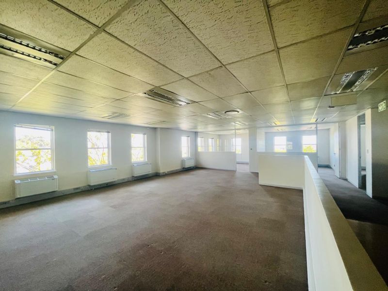 An open-plan commercial office space featuring a suspended ceiling, recessed lighting, wall-mounted HVAC units, and carpeted flooring.