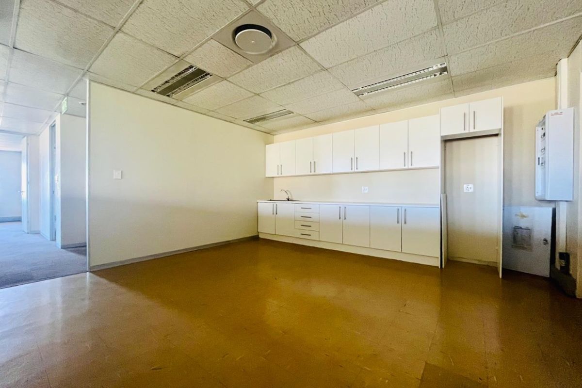 A functional commercial kitchenette featuring white built-in cabinetry, a sink, and a drop ceiling with integrated lighting.