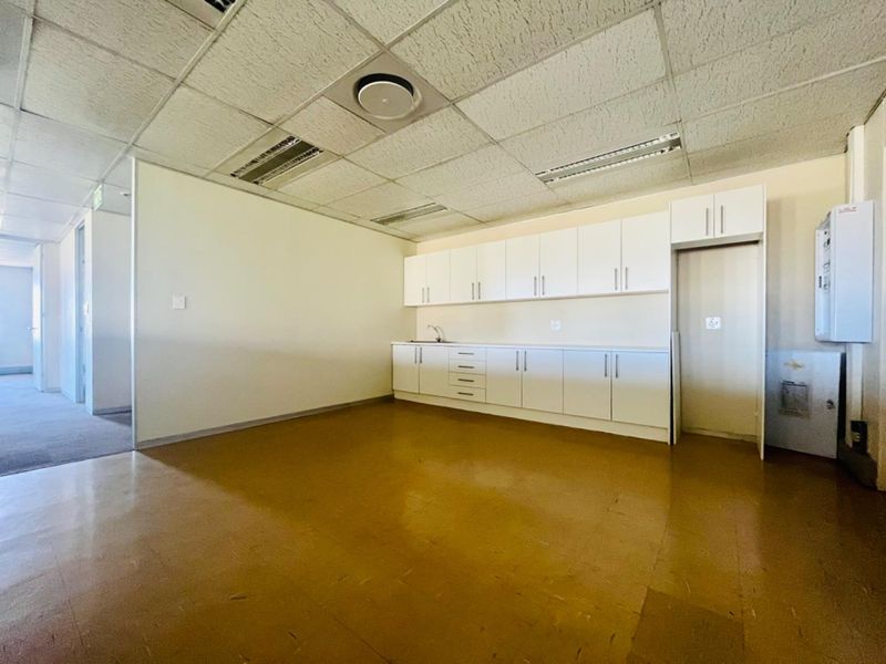 A functional commercial kitchenette featuring white built-in cabinetry, a sink, and a drop ceiling with integrated lighting.
