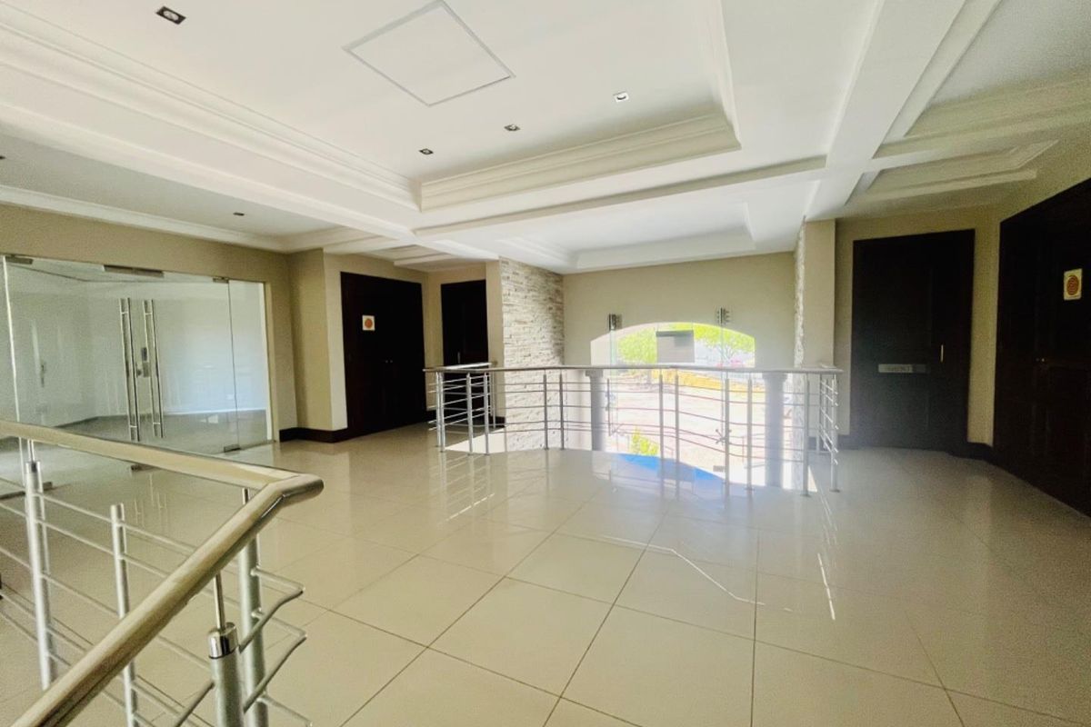 Spacious commercial hallway featuring tiled flooring, recessed ceiling lighting, a stone-clad feature wall, and modern stainless steel balustrades.