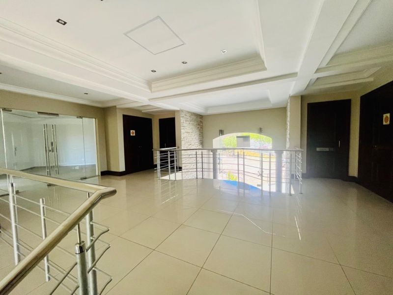 Spacious commercial hallway featuring tiled flooring, recessed ceiling lighting, a stone-clad feature wall, and modern stainless steel balustrades.