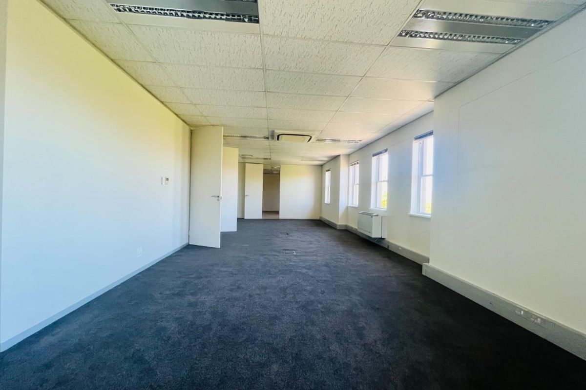 A vacant, open-plan commercial office space featuring dark carpeting, suspended ceilings with recessed lighting, and perimeter trunking for electrical and data connectivity.