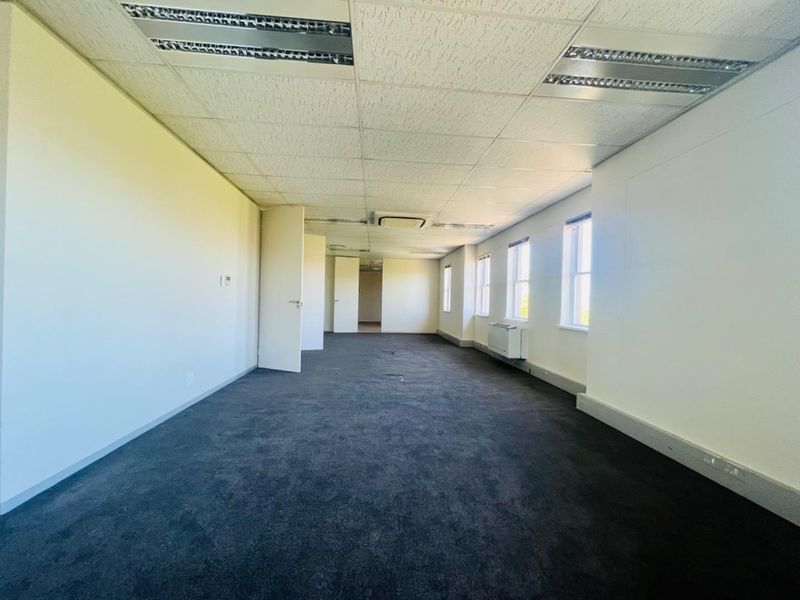 A vacant, open-plan commercial office space featuring dark carpeting, suspended ceilings with recessed lighting, and perimeter trunking for electrical and data connectivity.