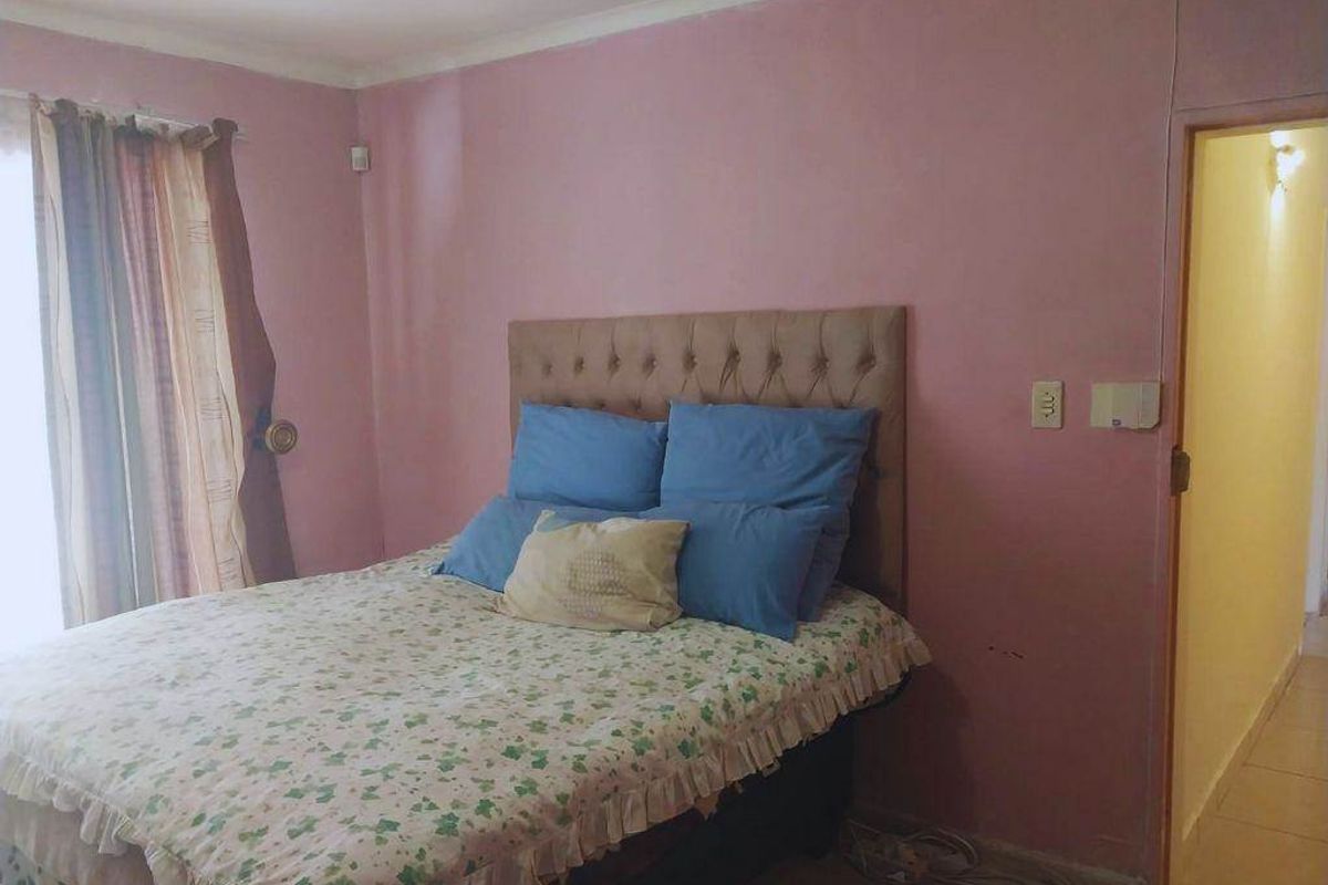 A bedroom featuring pink walls, tiled flooring, and a doorway leading to a hallway.