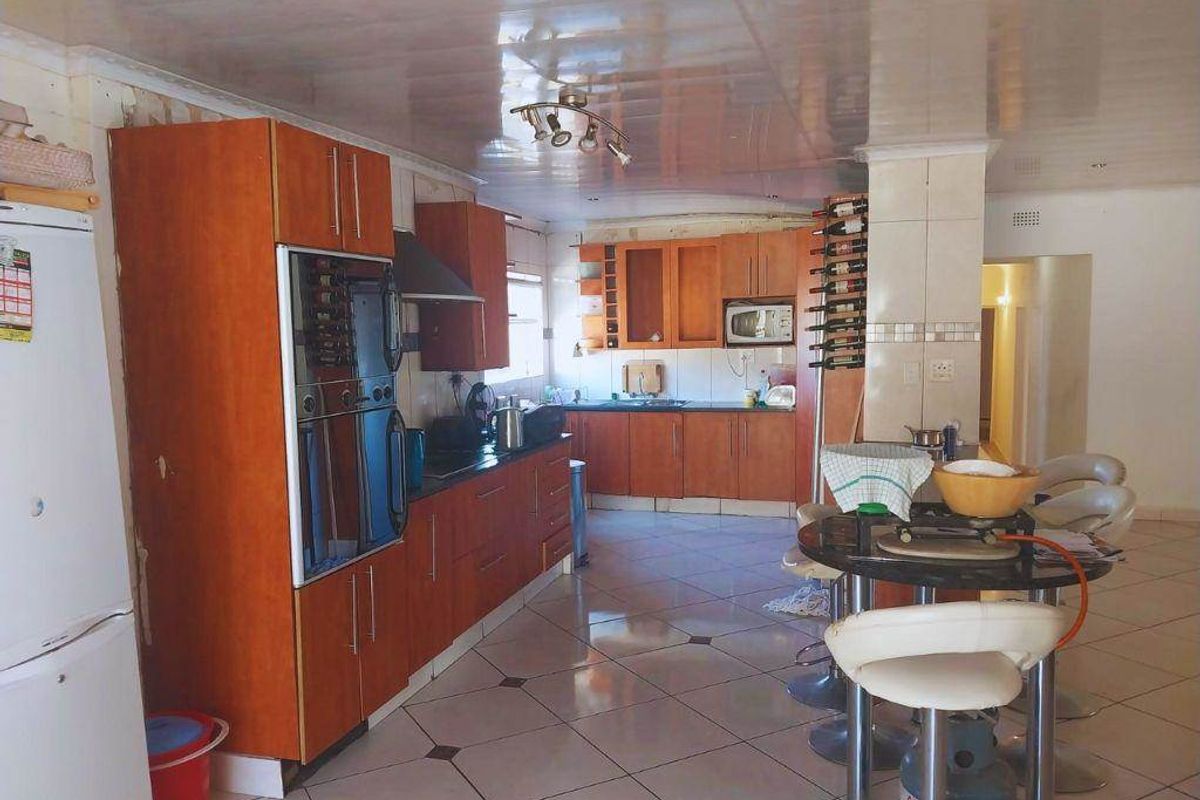 A dated kitchen featuring wood-veneer cabinetry, tiled flooring, and a glossy ceiling finish, offering a functional layout with built-in oven and hob.