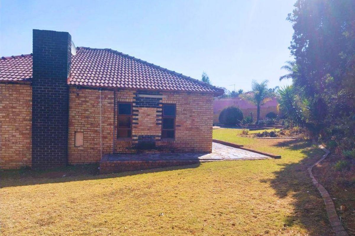 Rear view of the house featuring a brick facade, tiled roof, chimney, and a paved patio area overlooking the garden.