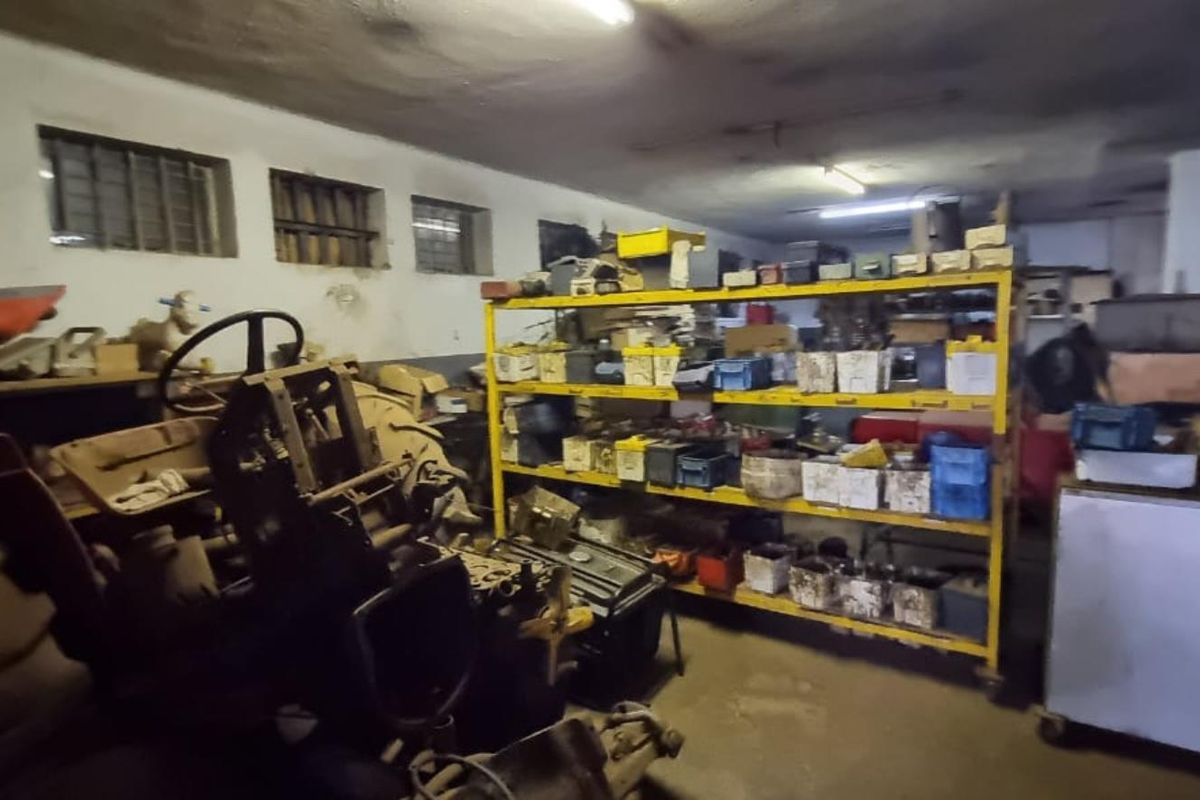 A utility space or storage area featuring industrial shelving, fluorescent lighting, and small high-level windows with security bars.