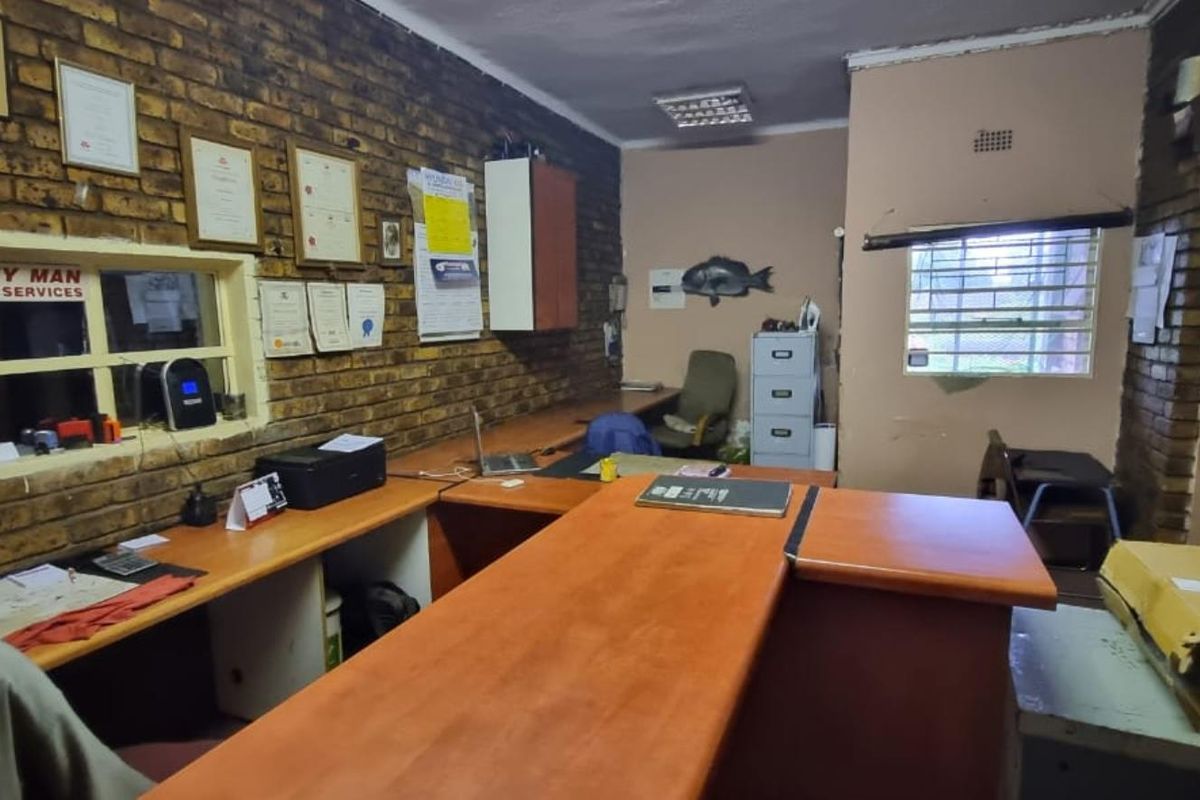 A functional commercial office space featuring exposed brick walls, built-in wooden desk counters, and security bars on the windows.