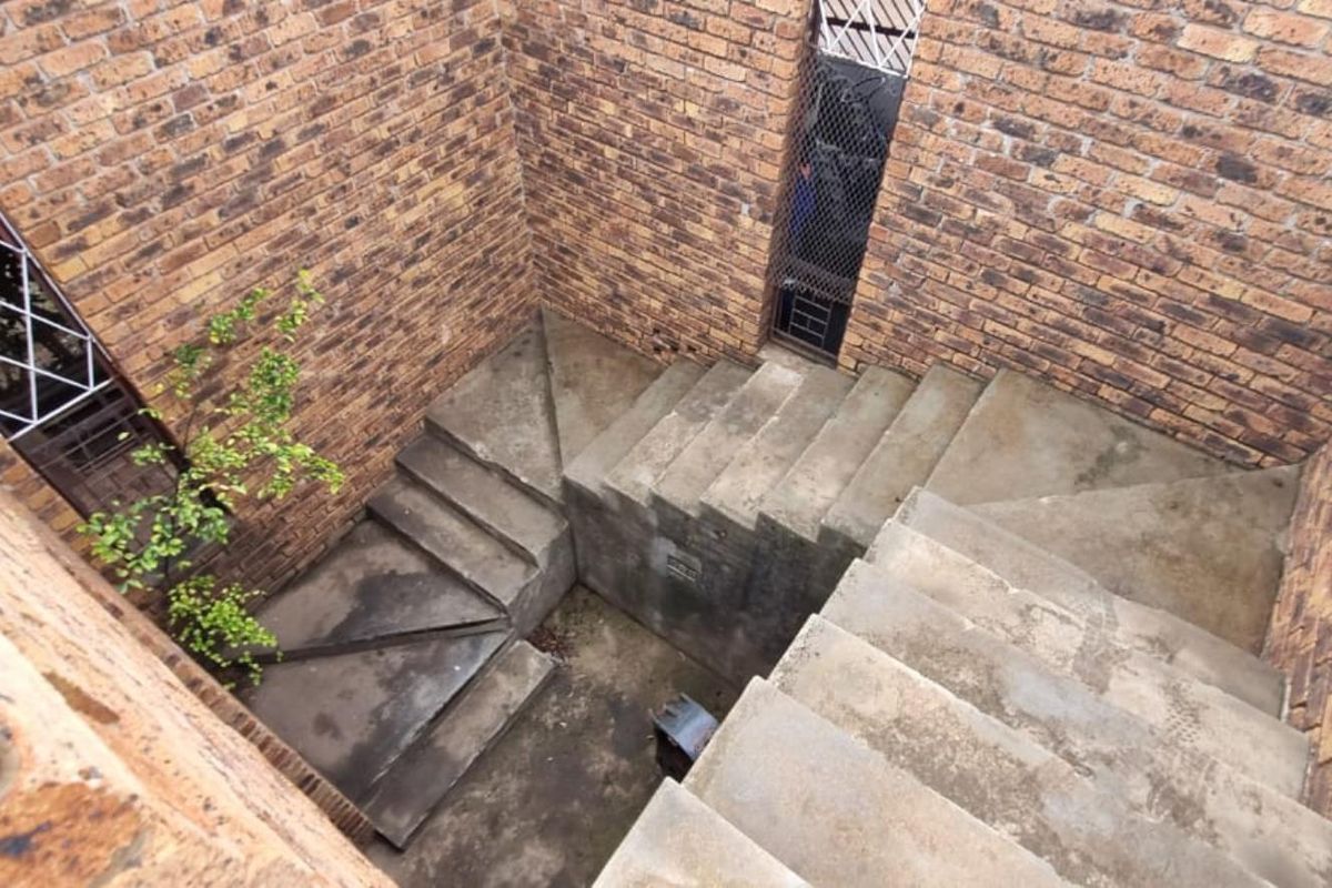 An exterior concrete stairwell enclosed by face brick walls, featuring security grilles on the windows.