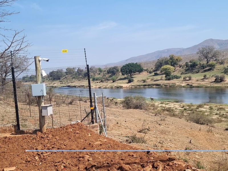 A view of the riverfront land featuring an electric security fence, surveillance cameras, and natural landscape surroundings.