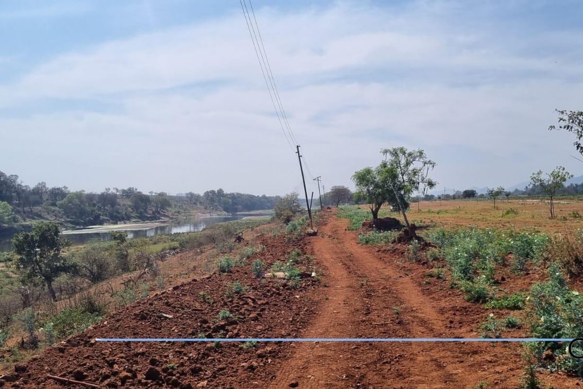 A view of the vacant residential land featuring a dirt access path, natural vegetation, and proximity to a riverbank.