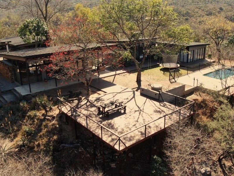 Aerial view of a modern bushveld property featuring a large elevated wooden deck, swimming pool, and expansive natural surroundings.