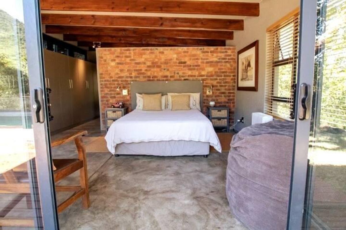 Spacious bedroom featuring exposed brick feature wall, polished concrete flooring, and exposed timber ceiling beams with large sliding glass doors.